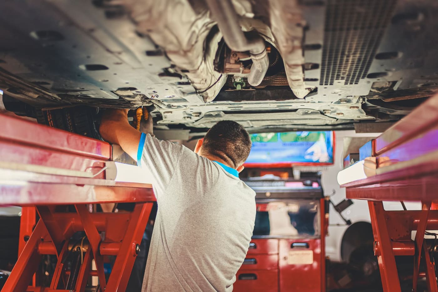 A mechanic working underneath a car raised on a workshop lift